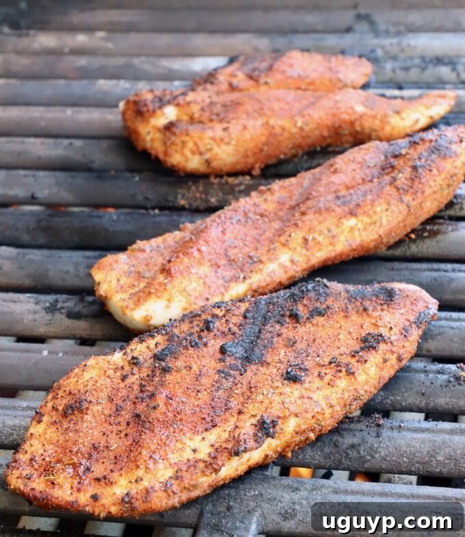 Seasoned boneless, skinless chicken breasts grilling over medium-high heat, showing char marks and even cooking.