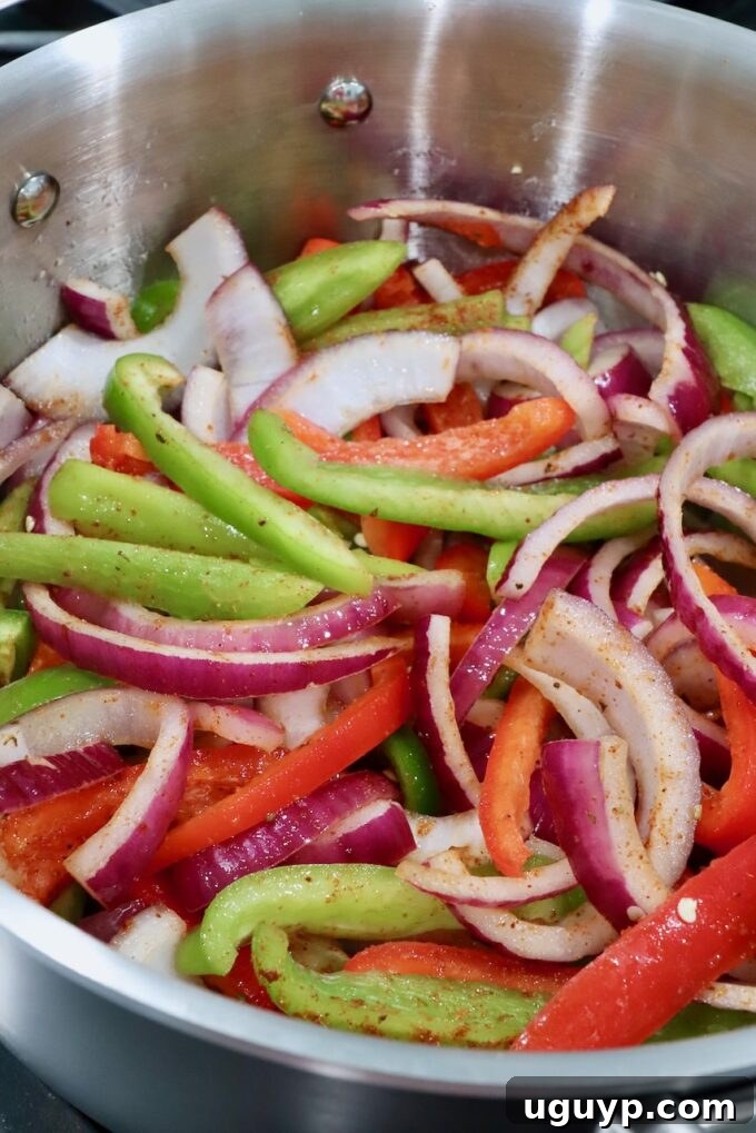 Sliced red and green bell peppers, and red onions cooking in a large skillet, softened and slightly caramelized.