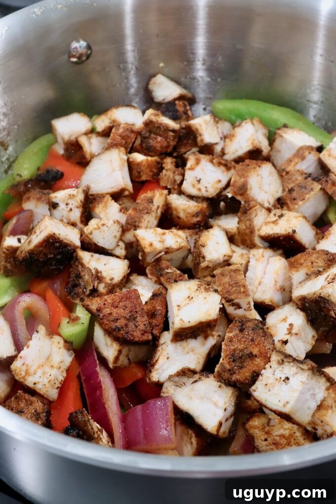Diced grilled chicken mixed with sautéed fajita vegetables (bell peppers, onions, jalapenos) in a skillet, ready for quesadilla assembly.