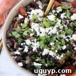 Mexican black beans in a bowl, topped with crumbled cheese and fresh cilantro, ready to be served.