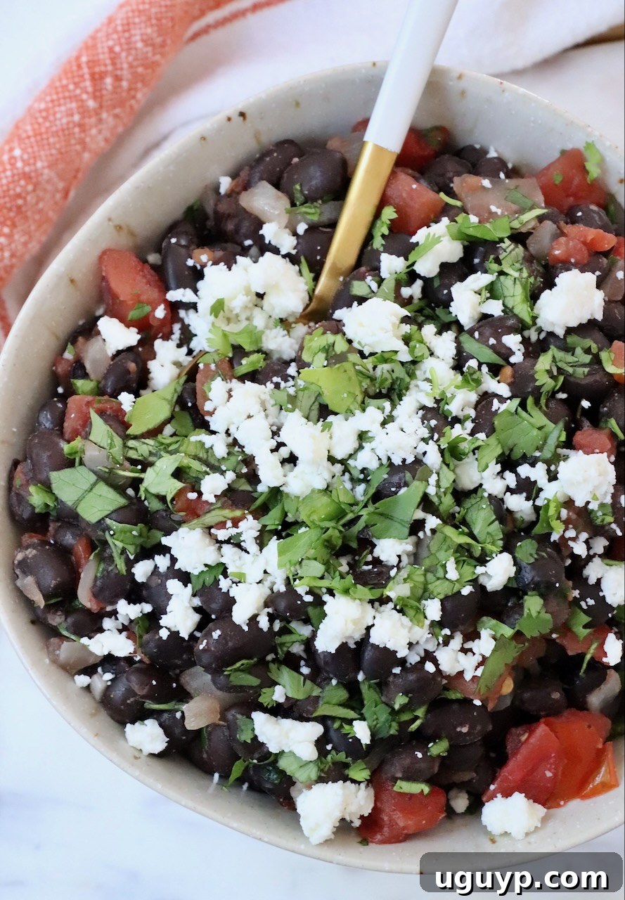 A close-up view of cooked Mexican black beans in a bowl, showing a spoon resting inside, highlighting their rich, saucy texture.
