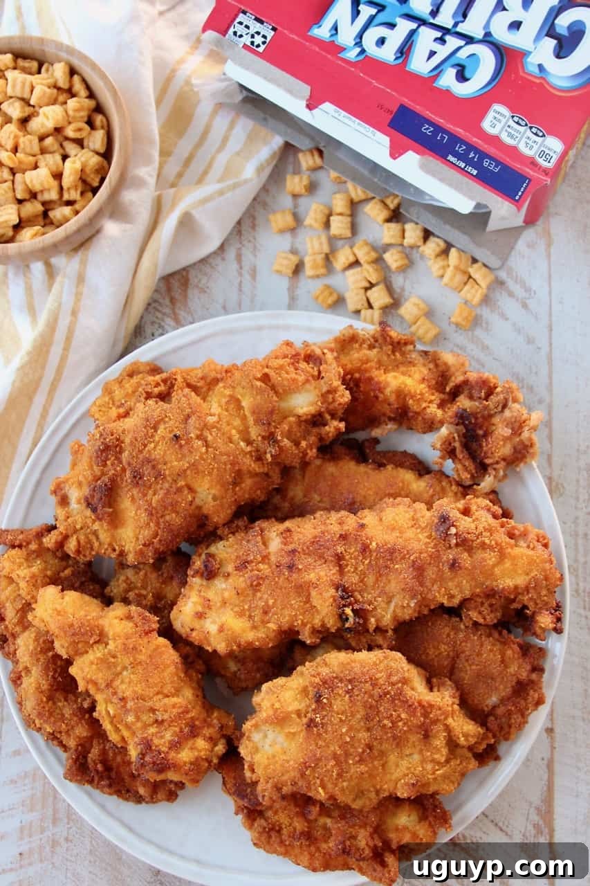 Crispy Captain Crunch Fried Chicken tenders stacked on a plate, with a box of Captain Crunch cereal in the background, highlighting the unique breading.