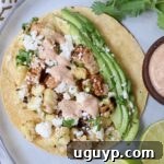 taco on plate topped with diced chicken, corn kernels and avocado slices