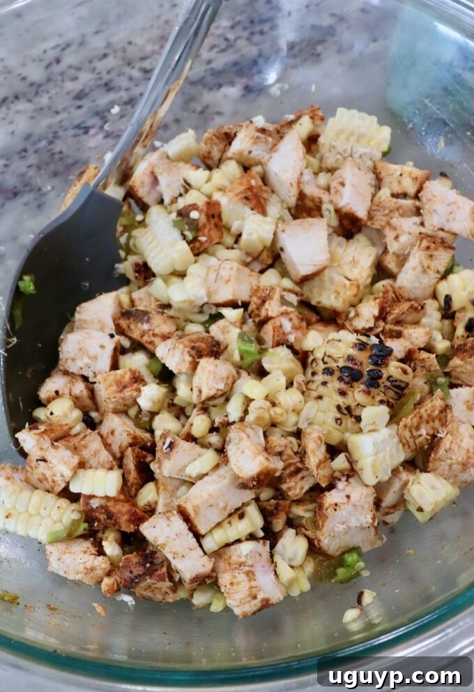 diced grilled chicken, corn kernels and diced jalapenos in glass bowl with mixing spoon