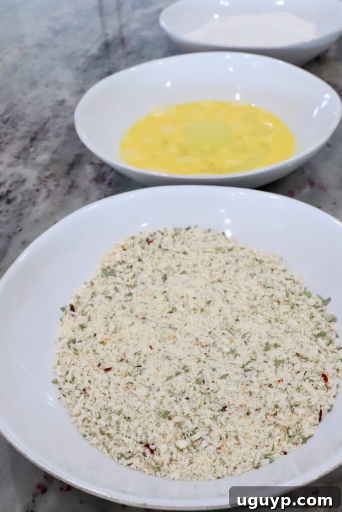 Three shallow bowls filled with seasoned breadcrumbs, whisked eggs, and flour, arranged for breading.