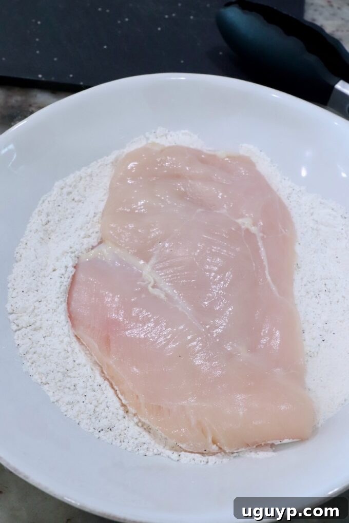 A chicken breast being coated in a bowl of all-purpose flour.