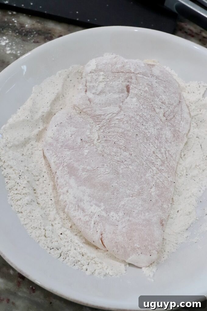 A chicken breast fully coated in flour, ready for the next step.