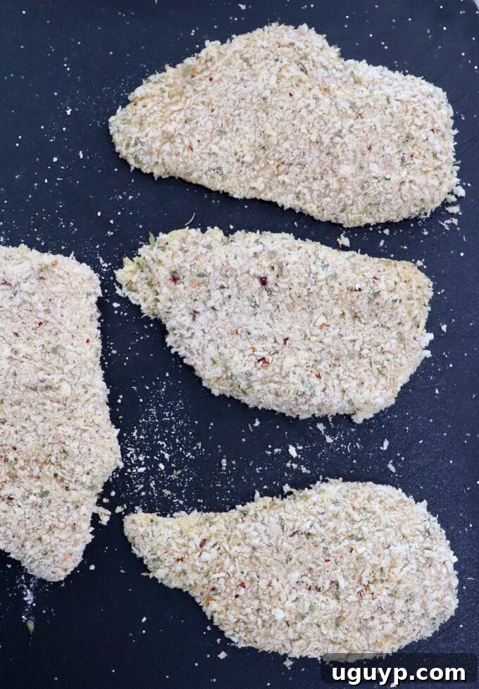 Several breadcrumb-coated chicken breasts laid out on a cutting board, ready for cooking.