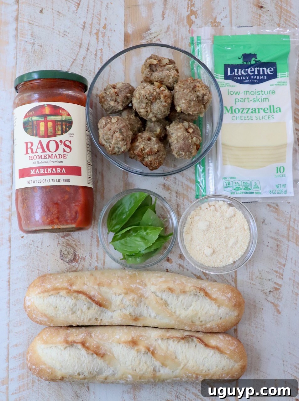 Ingredients for homemade meatball subs laid out on a white wooden board.