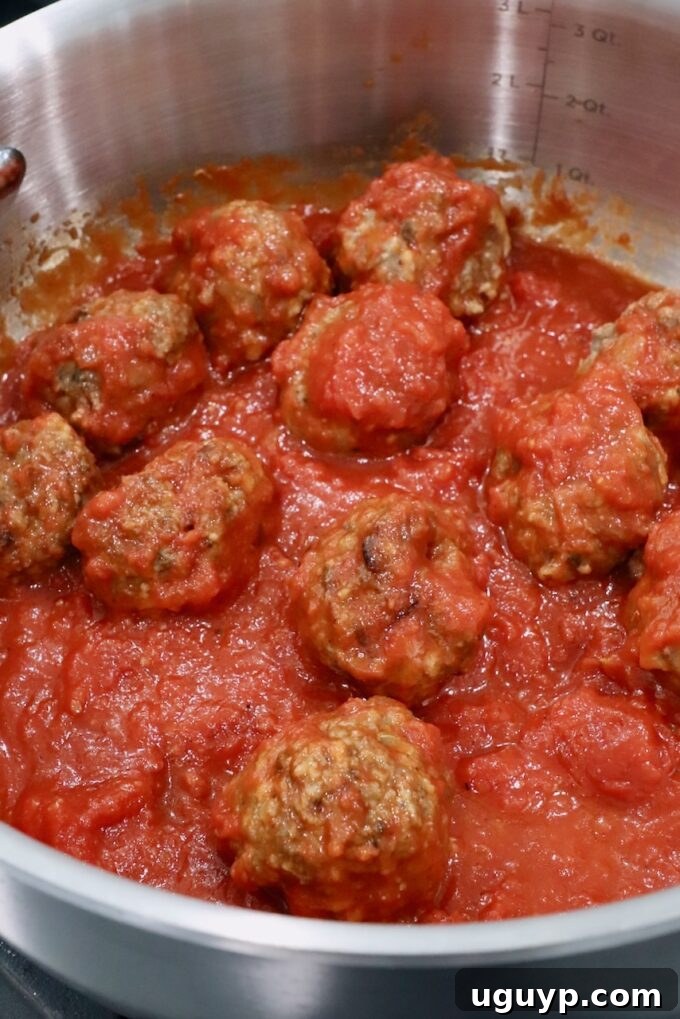 Meatballs simmering in rich marinara sauce in a large pan on the stove.
