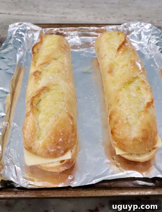 Baguettes filled with mozzarella cheese on a foil-lined baking sheet, ready for the oven.
