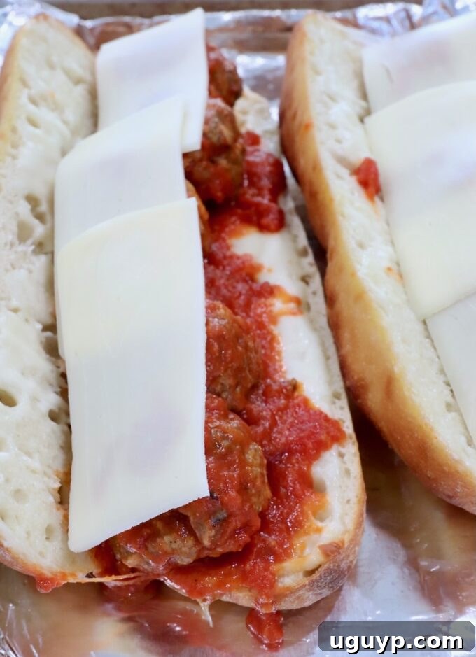 Meatball sub topped with additional slices of mozzarella cheese, ready for final melting.