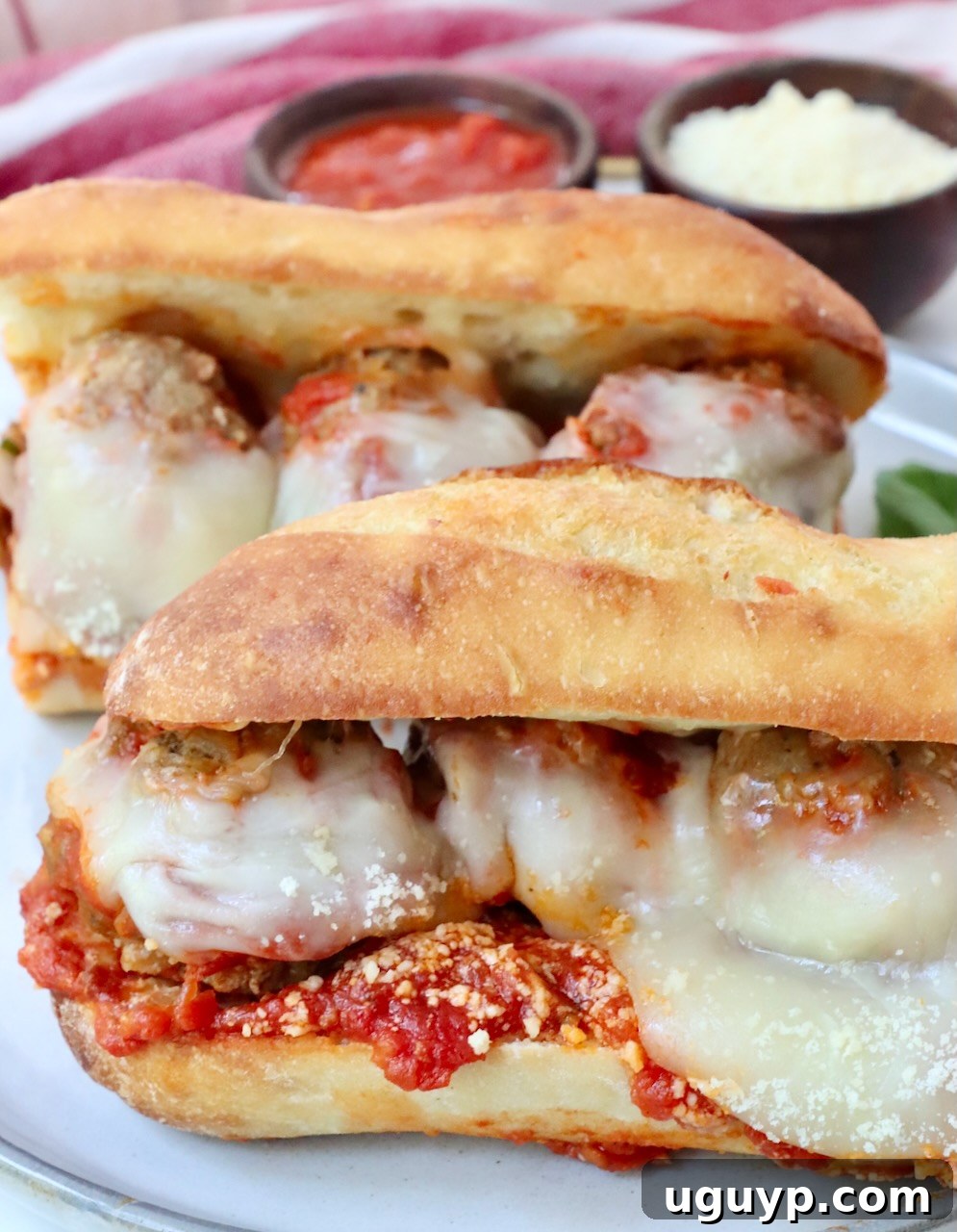 Two meatball sub sandwiches served on a white plate, garnished with basil.