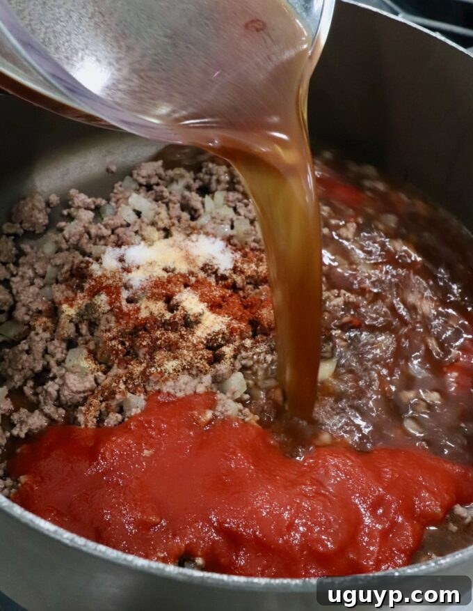 beef broth poured into a pot with cooked ground beef, spices and tomato sauce