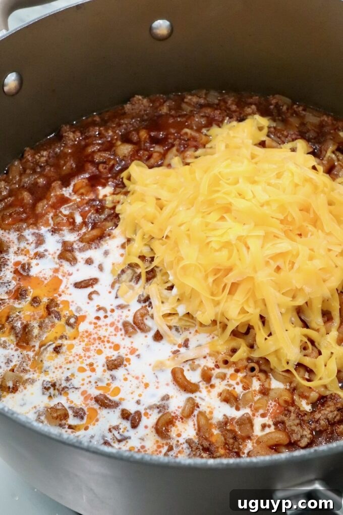 shredded cheddar cheese and heavy cream in a pot of cooked ground beef, noodles and sauce