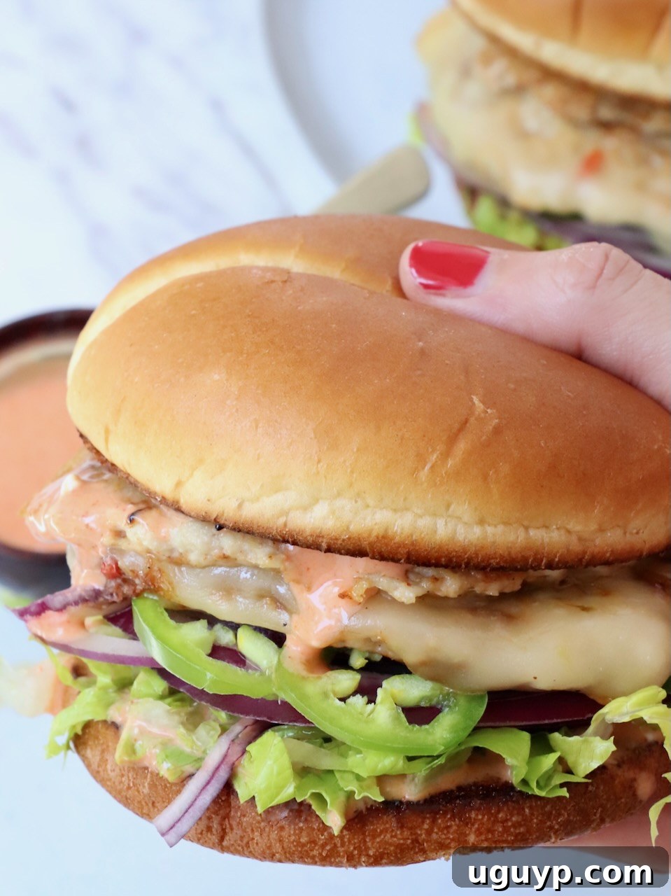 hand holding a perfectly crafted buffalo chicken smash burger over a plate, showcasing its juicy patty, melted cheese, and fresh toppings.