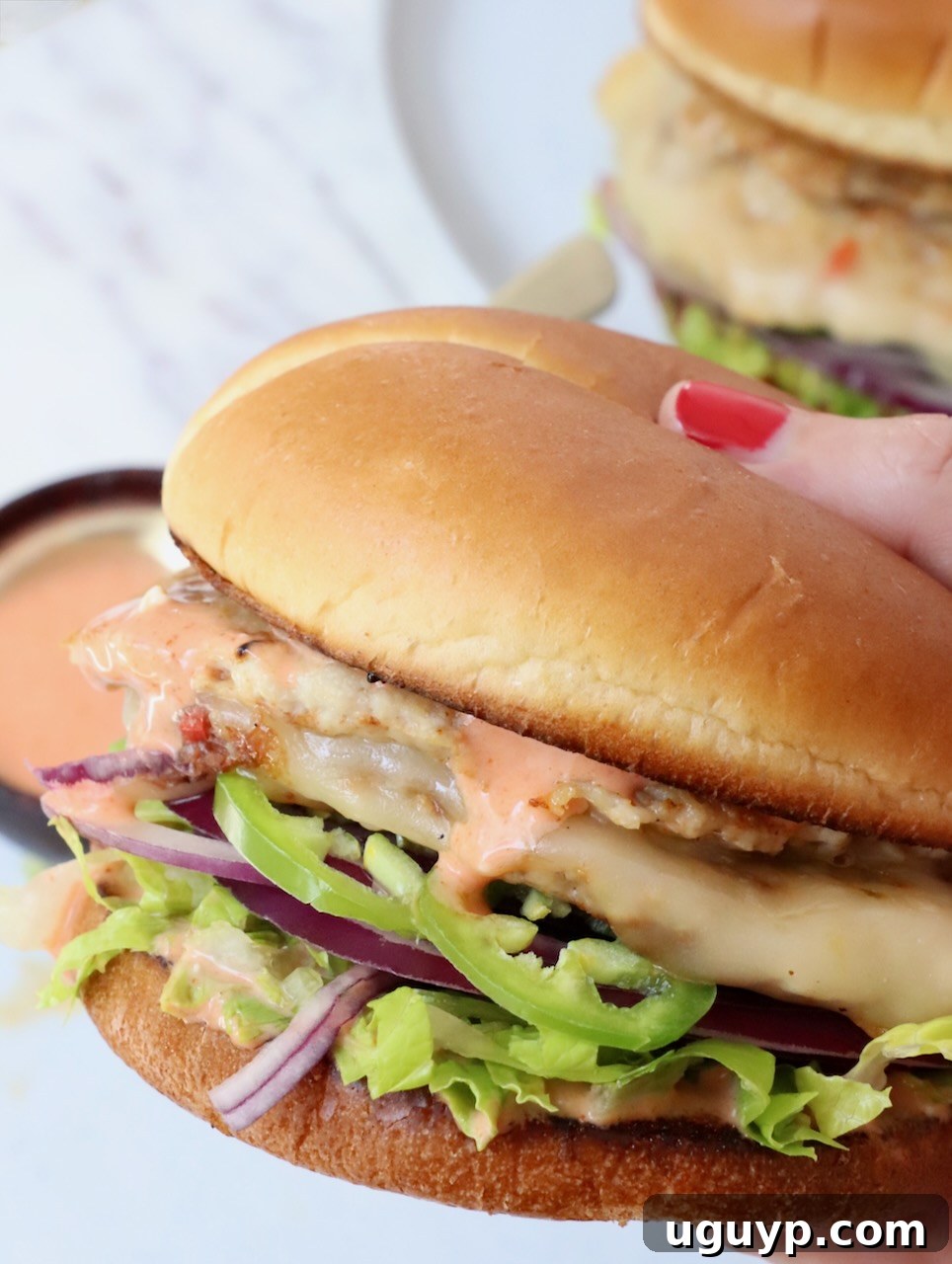 a close-up shot of a hand holding a buffalo chicken smash burger, showing its enticing layers of chicken, cheese, and toppings