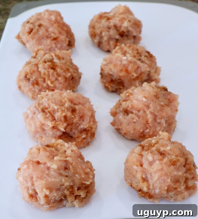seasoned balls of ground chicken on a white cutting board, ready to be smashed