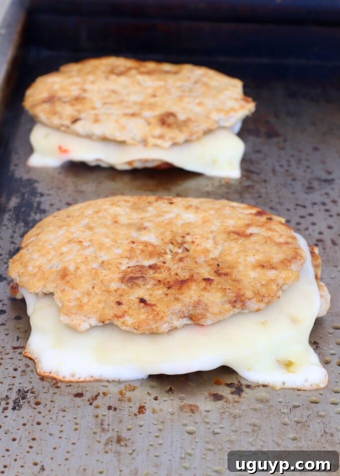 stacked cooked chicken burger patties with slices of melted pepper jack cheese on a griddle