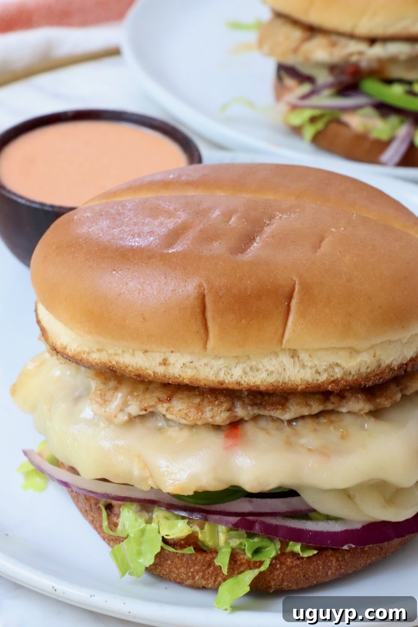 a single buffalo chicken smash burger on a plate, served with a small bowl of buffalo sauce on the side for dipping