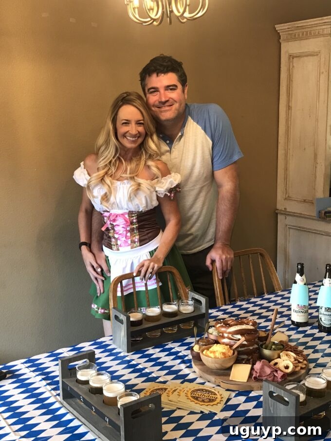 A man and woman dressed in traditional German attire (Lederhosen and Dirndl) at an Oktoberfest themed party setup.