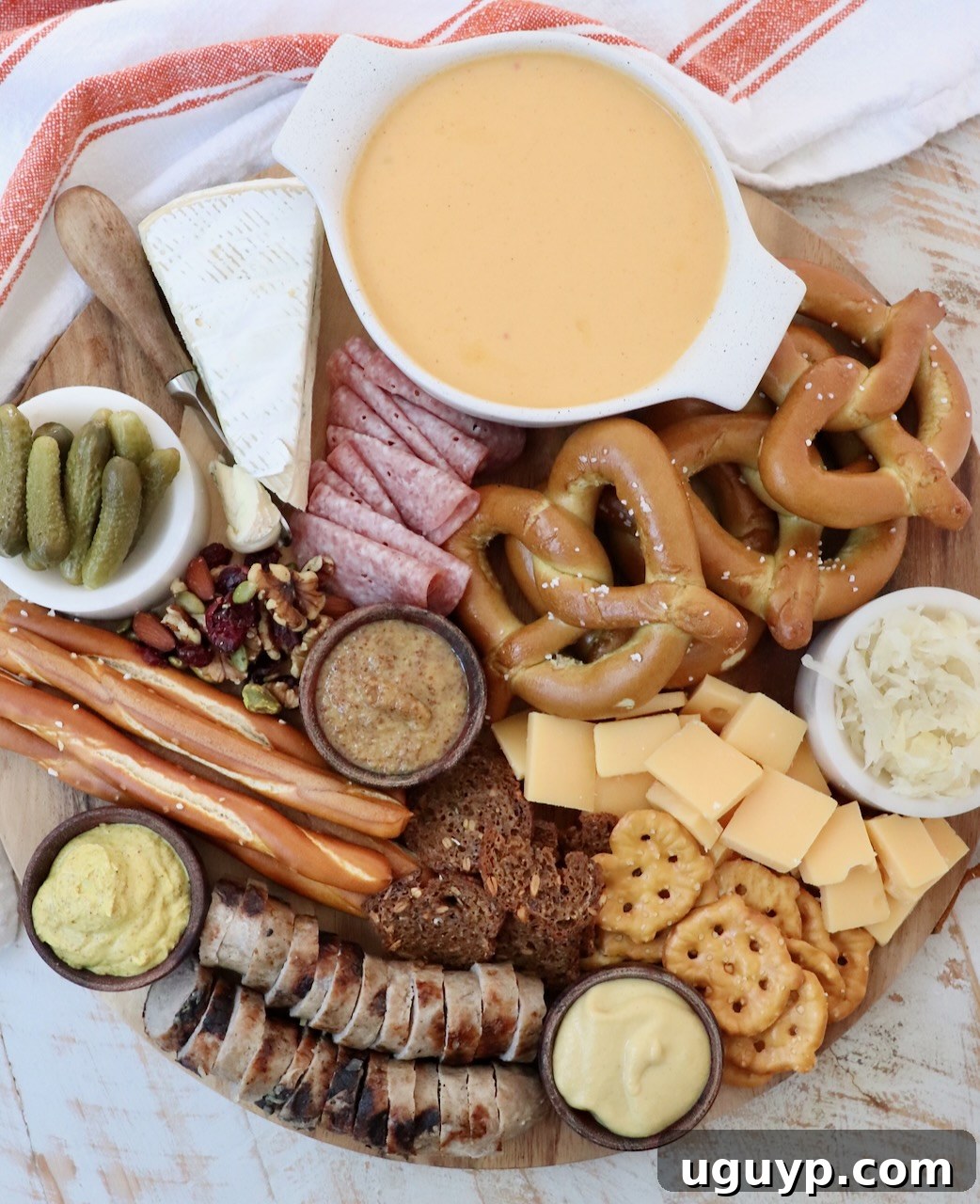 A grand Oktoberfest charcuterie board overflowing with various cheeses, a selection of cooked meats, and an array of pretzels and crackers.