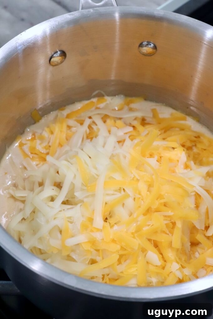 shredded cheese added to a creamy sauce in a pot on the stove