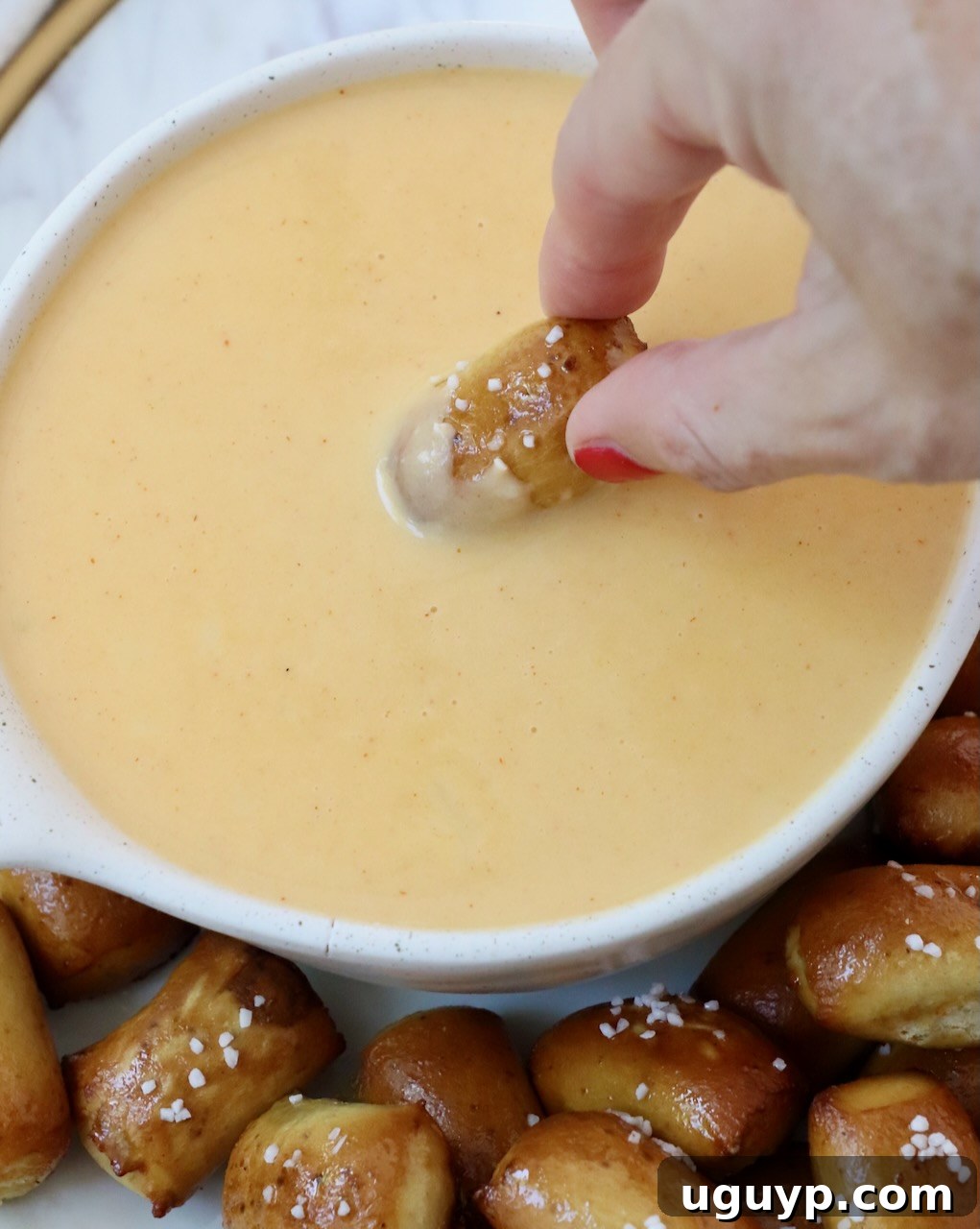 hand dipping pretzel bite into beer cheese dip