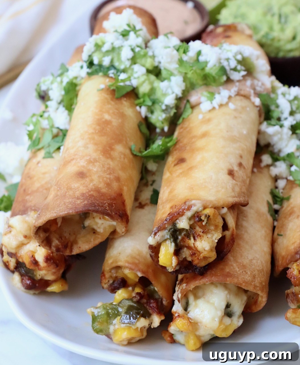 Crispy Mexican Street Corn Taquitos stacked on a plate, showcasing their cheesy, corn-filled interior