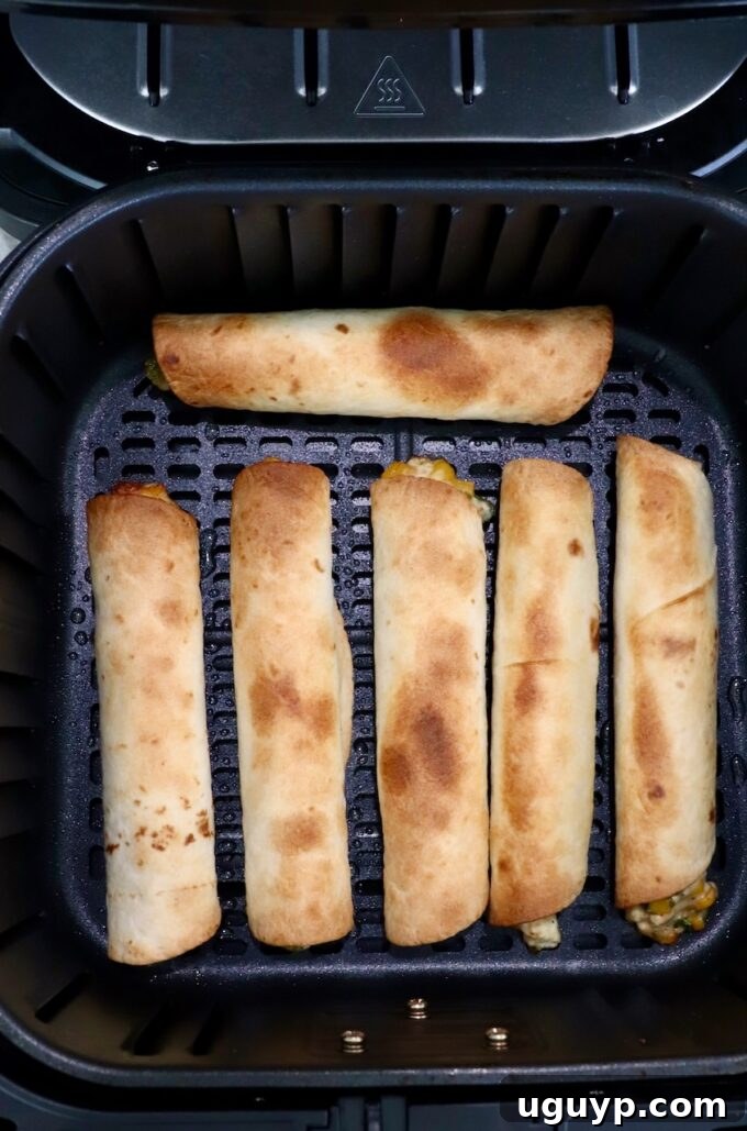 Golden brown, crispy cooked taquitos nestled in an air fryer basket, fresh out of cooking