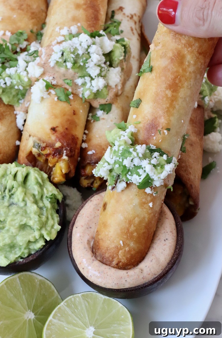 A hand dipping a crispy Mexican street corn taquito into a small bowl of chili lime sauce