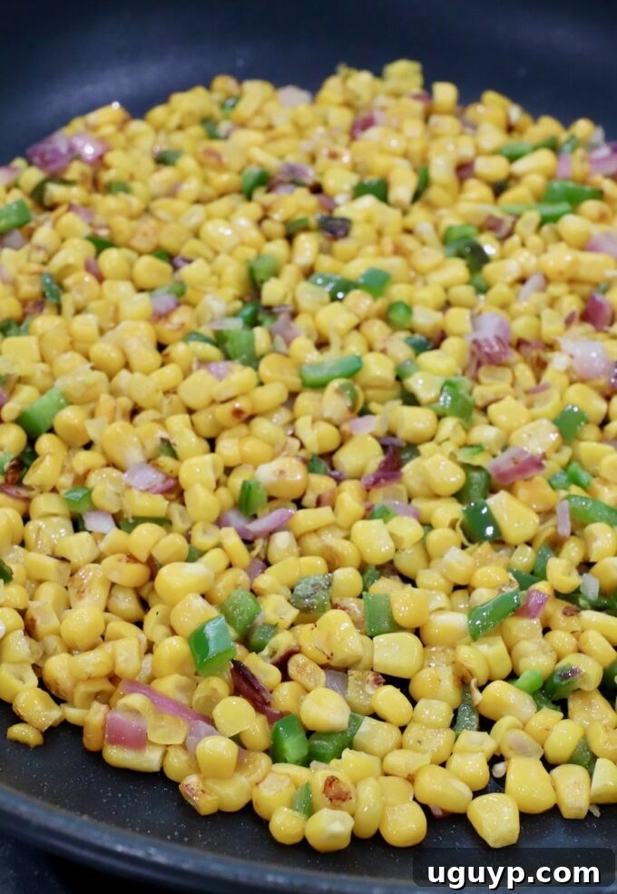 Skillet with perfectly charred corn kernels, diced red onions, and jalapeños, ready for the next step