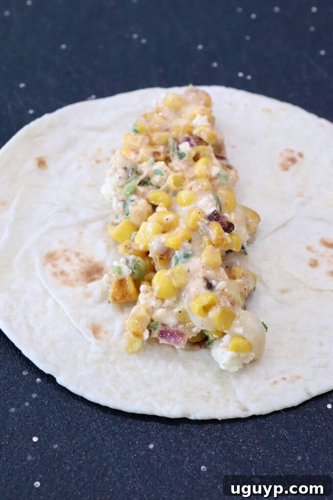 Creamy corn mixture perfectly centered on a warm tortilla on a cutting board, ready for rolling