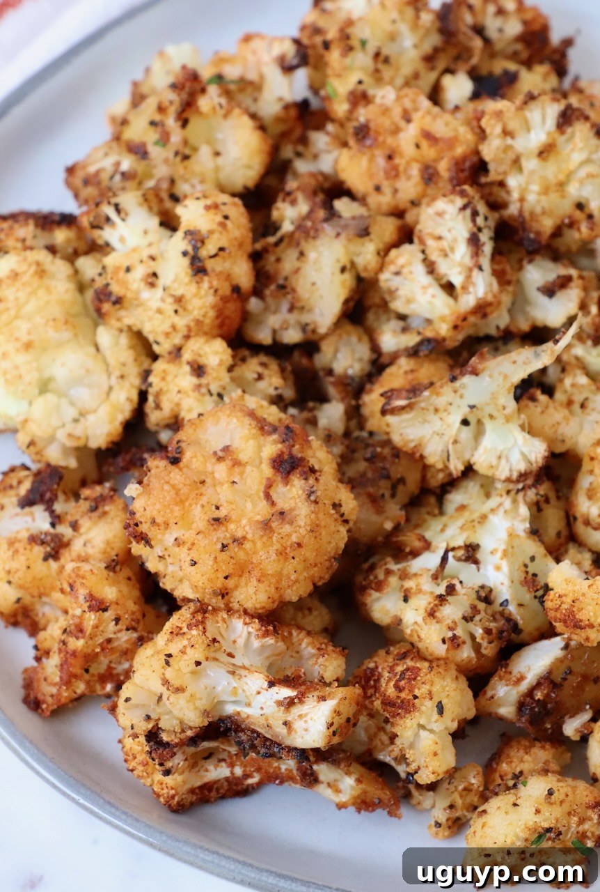 A plate of perfectly roasted cauliflower florets, golden brown and garnished slightly.