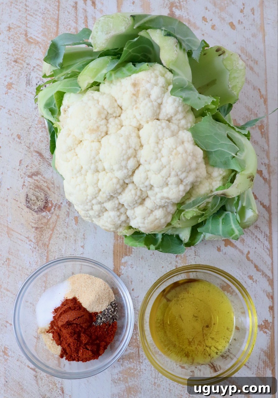 A head of fresh cauliflower next to small bowls of olive oil and mixed spices, ready for preparation.