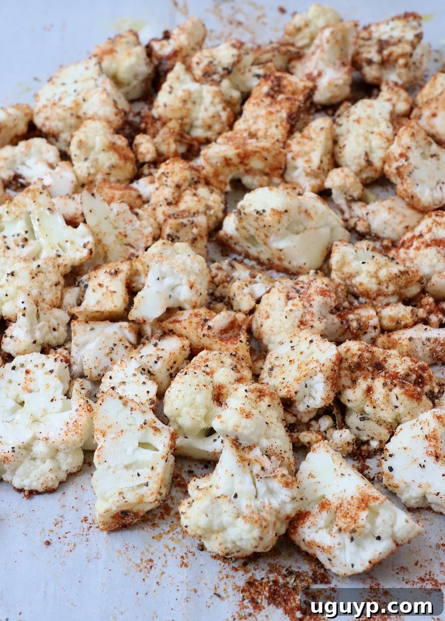 Seasoned cauliflower florets spread in a single layer on a parchment-lined baking sheet, ready for roasting.