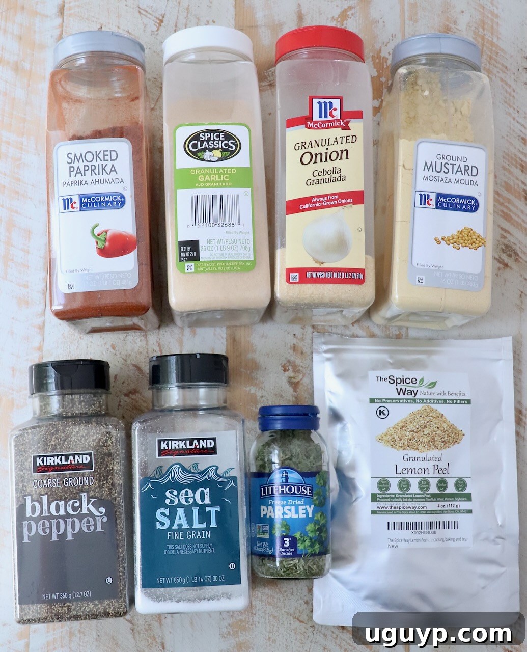 An organized display of various fresh and dried herbs and spices in clear containers and jars on a white wooden board, ready for a seasoning blend.
