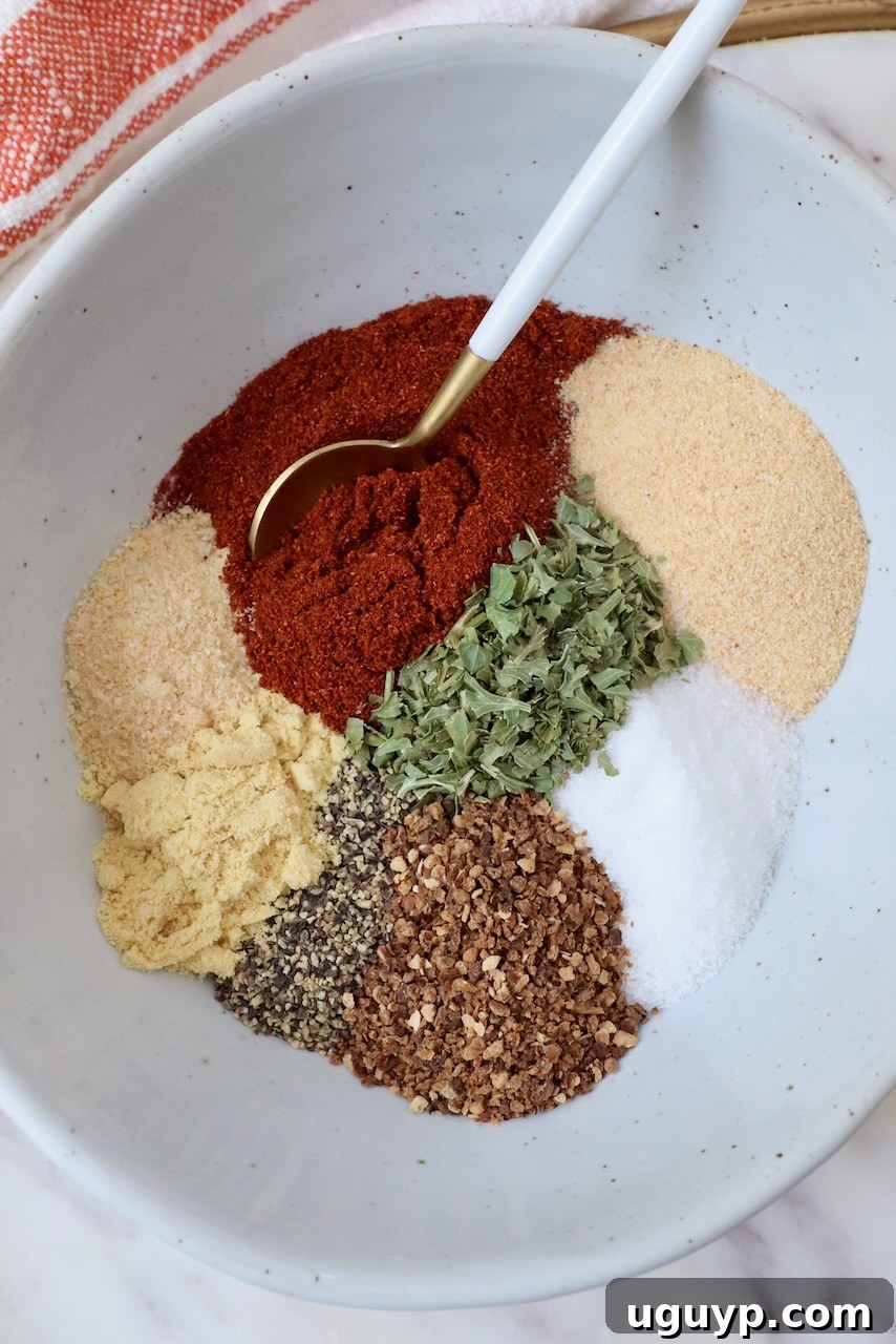 An array of individual spices and dried herbs, including smoked paprika, garlic powder, and dried lemon zest, thoughtfully separated in a bowl with a spoon.