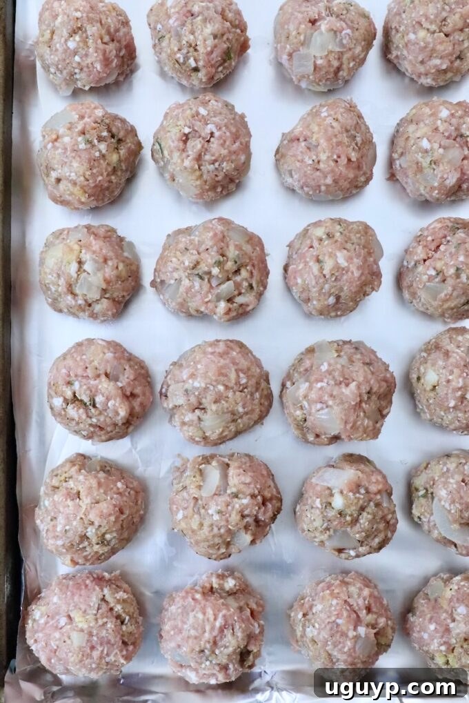 Uncooked turkey meatballs, perfectly shaped and arranged in a single layer on a foil-lined baking sheet, ready for the oven.