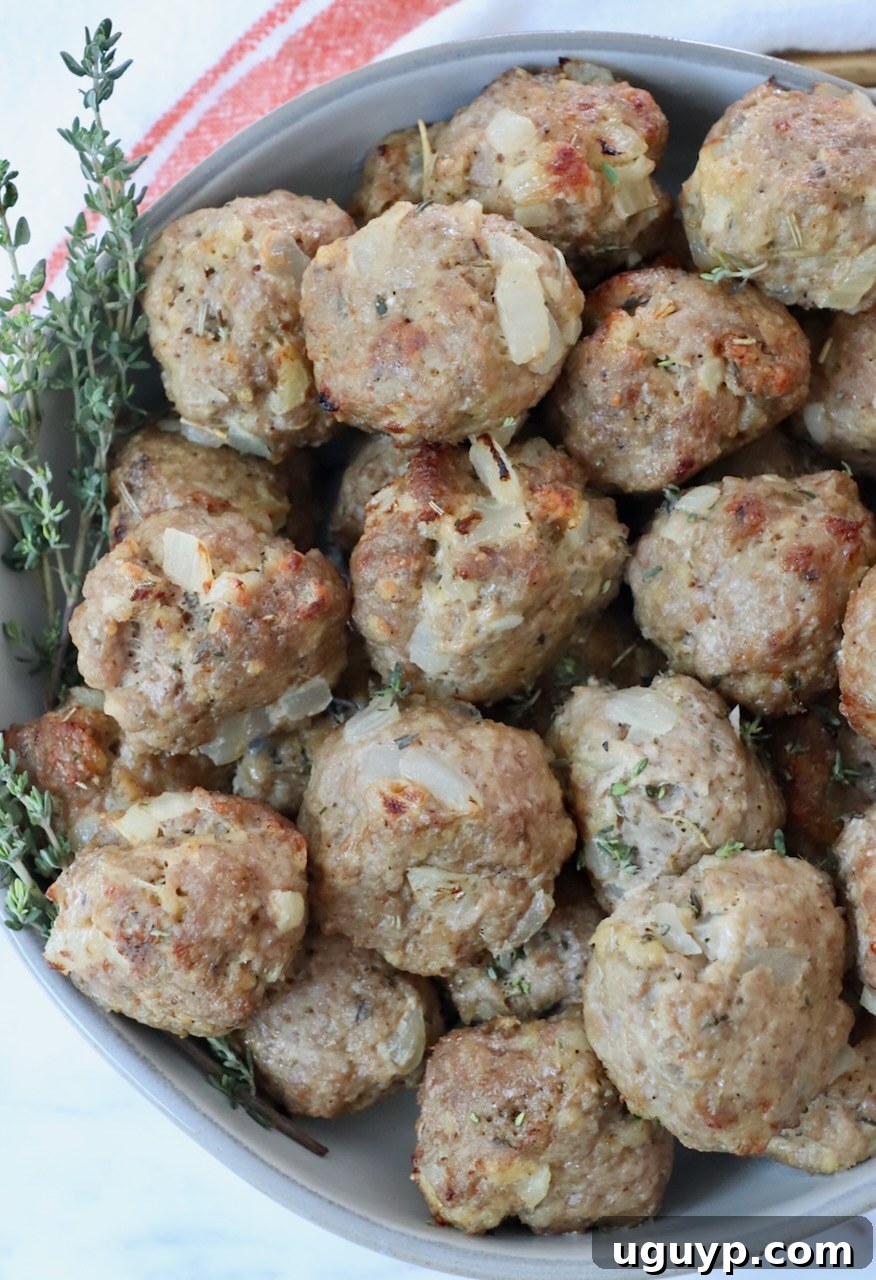 A stack of perfectly browned turkey meatballs in a bowl, garnished with fresh thyme, emphasizing their juicy interior.