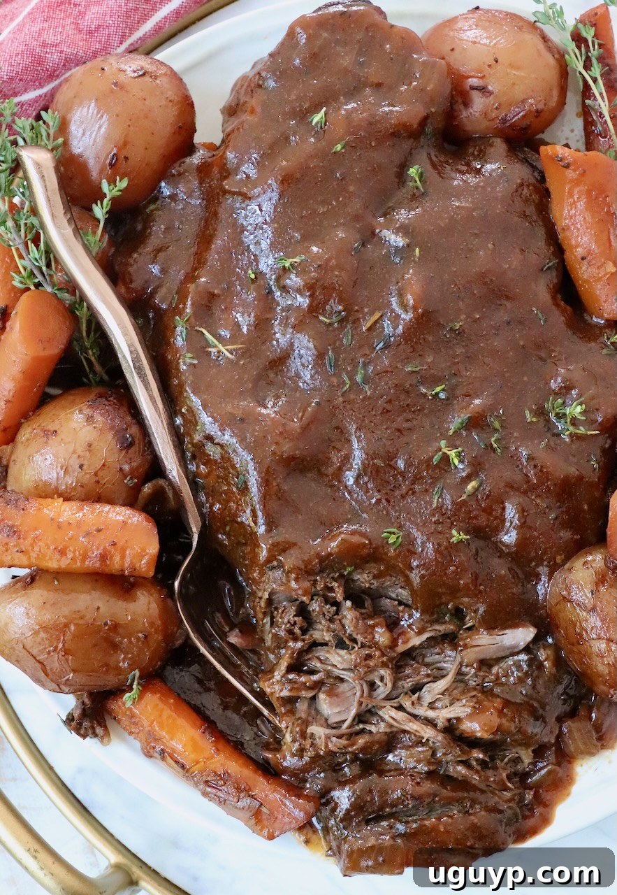 A perfectly cooked pot roast served on a rustic plate, surrounded by tender carrots, potatoes, and smothered in rich pan gravy, ready to be enjoyed.