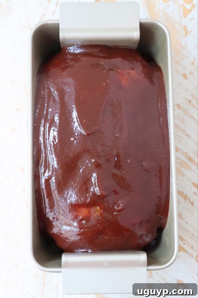Turkey meatloaf in a loaf pan, topped with a generous layer of BBQ sauce, before final baking.