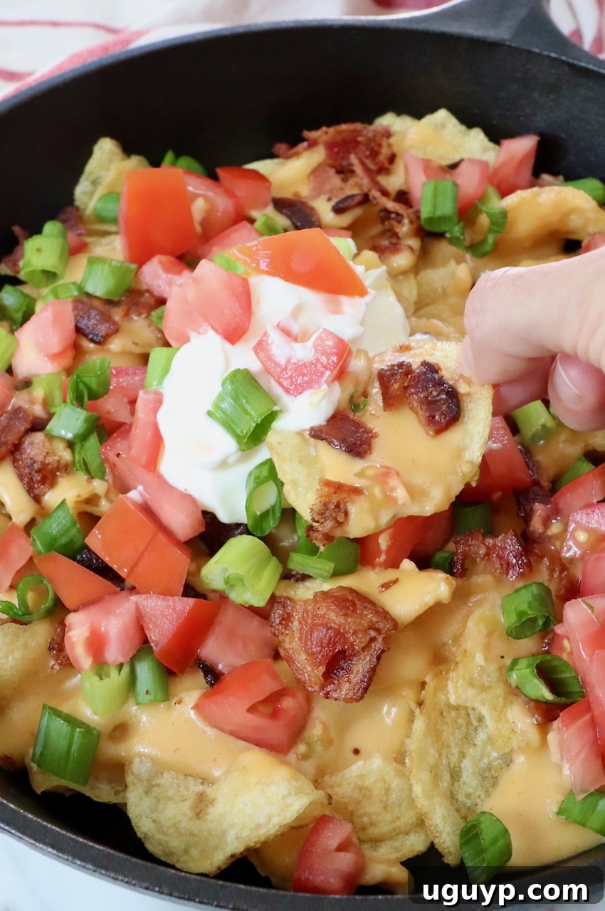 A cast iron skillet filled with golden Irish nachos, topped with a generous dollop of sour cream, ready to be served