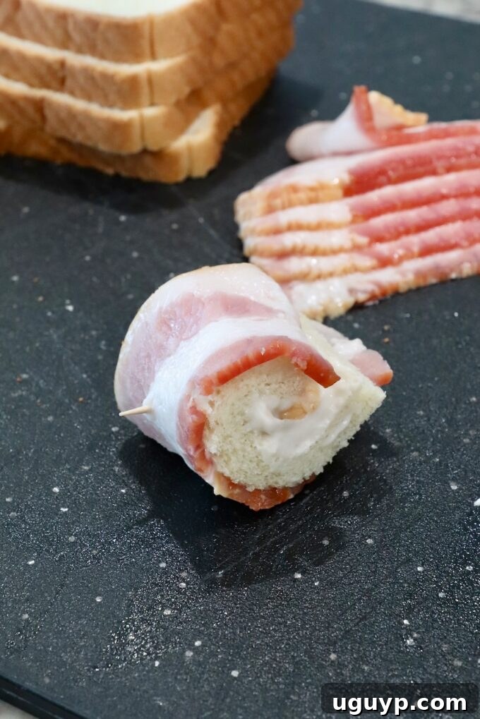 A bacon-wrapped bread roll-up secured with a toothpick, showcasing the assembly process of the appetizer.