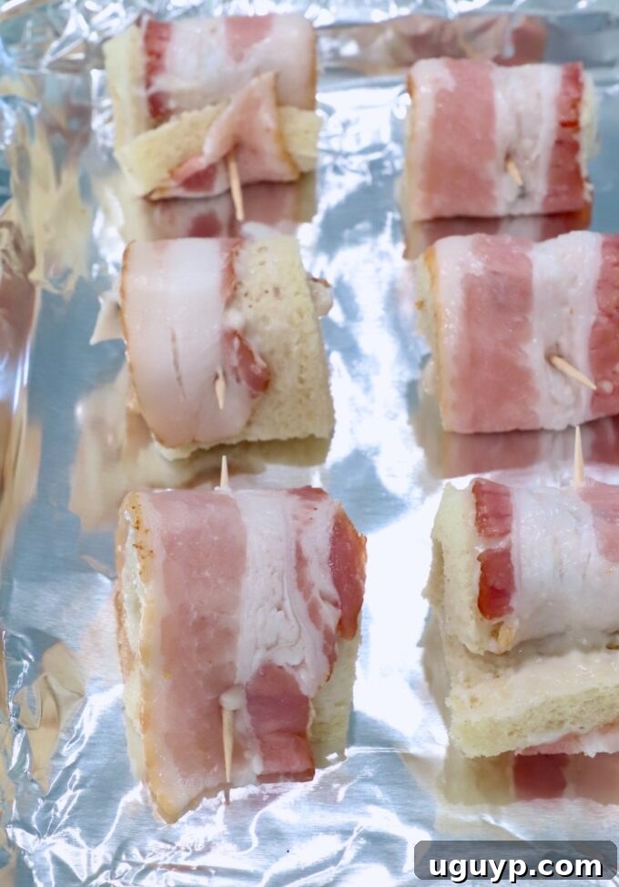 Assembled bacon roll ups arranged in neat rows on a foil-lined baking sheet, prepared for baking.