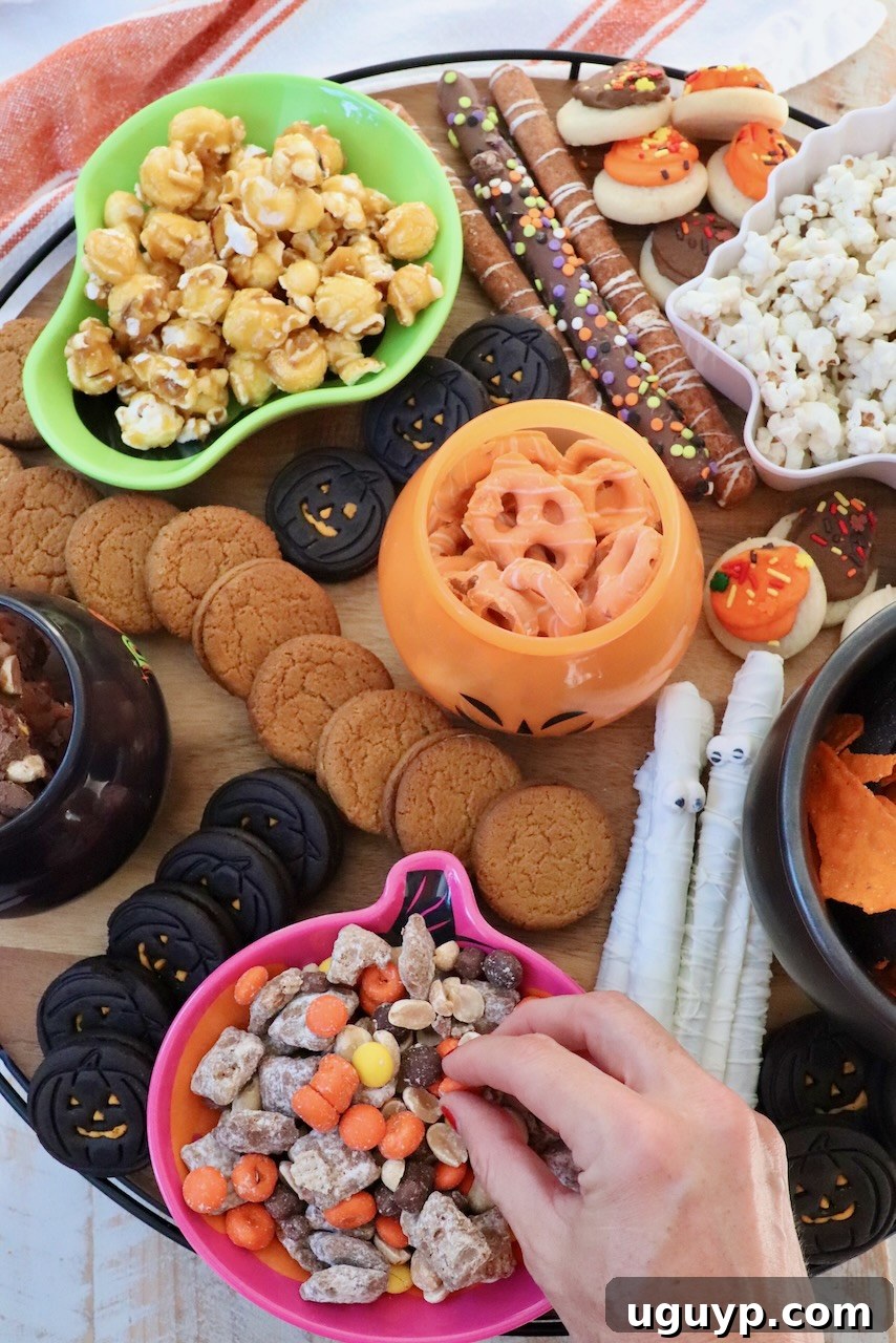 A festive Halloween snack board featuring an array of small bowls filled with spooky and delicious snacks and cookies, perfect for a party.