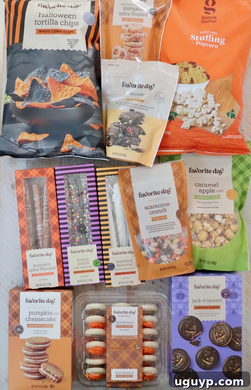 An assortment of Halloween-themed snacks and cookies displayed in their original boxes and bags on a white wooden table, showcasing the variety available for the snack board.
