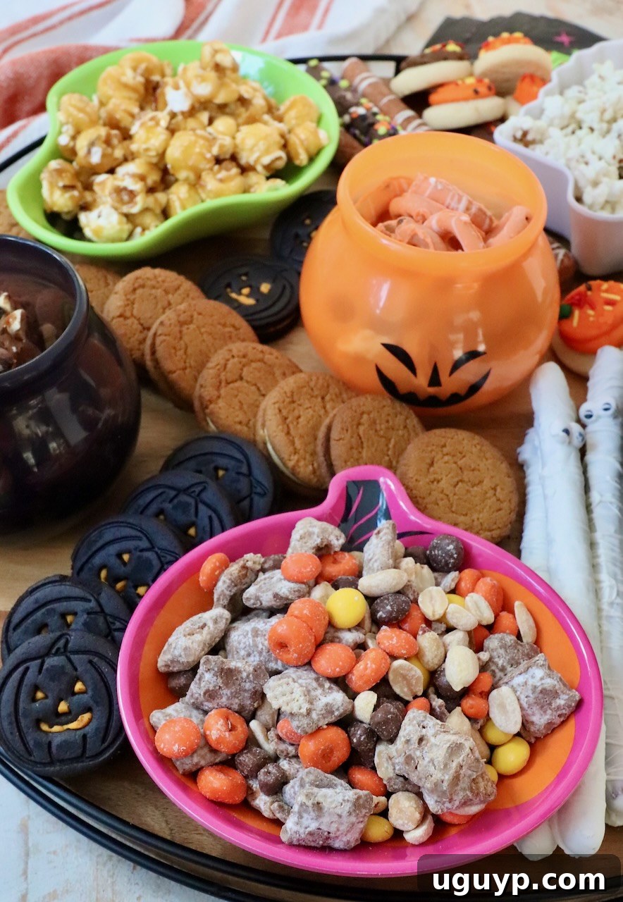 A close-up view of a Halloween snack board featuring small bowls filled with colorful snacks, alongside artfully arranged cookies and pretzel rods, creating a rich and inviting display.