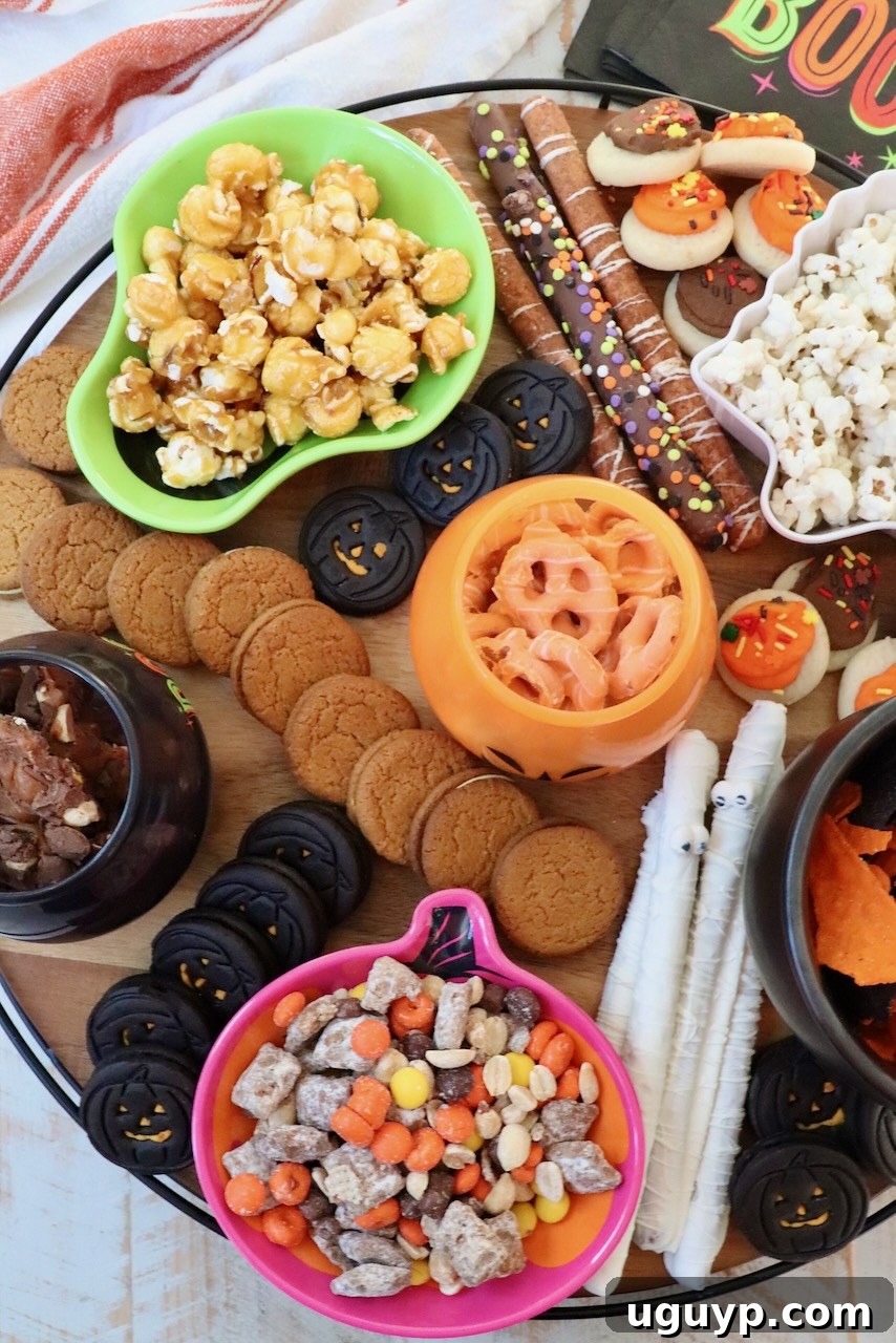 A vibrant Halloween snack board filled with a variety of themed bowls of pretzels, candies, and popcorn, expertly arranged with cookies for a perfect party display.