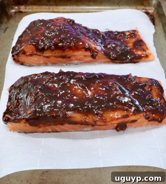 Unbaked balsamic glazed salmon placed on a piece of parchment paper on a baking sheet, ready for the oven.